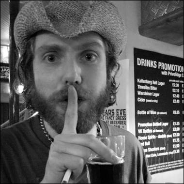 A person in a cowboy hat holding a cigarette and a drink
Description automatically generated