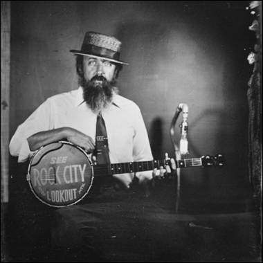 A person with a beard and a hat holding a banjo
Description automatically generated