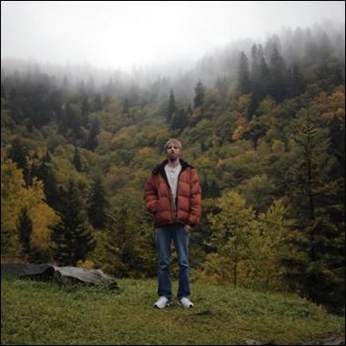 A person standing on a hill with trees in the background
Description automatically generated
