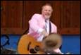 A person in a pink suit playing a guitar

Description automatically generated